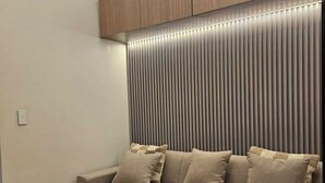 A modern living room with a sectional sofa, a ceiling light fixture, and a wall panel. - Luxury condo with gym,WiFi,NETFLIX at Park Mckinley West, Venice, SM Aura BGC (Taguig)
