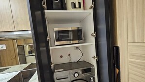 A compact kitchen with a microwave, toaster, and washing machine. - Luxury condo with gym,WiFi,NETFLIX at Park Mckinley West, Venice, SM Aura BGC (Taguig)