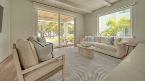Ein modernes Wohnzimmer mit einem großen Schiebeglasfenster, das auf einen Balkon führt, einer Couch, einem Couchtisch und einer Lampe.