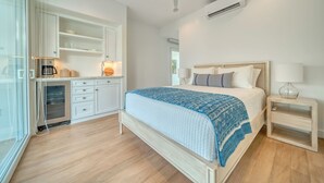 A bedroom with a bed, bedside table, and a kitchenette area.