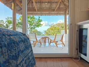 A balcony with a table and chairs, a TV, and a view of the sea. - Elevated Island Escape – Studio Condo with Ocean Views (Roatán)