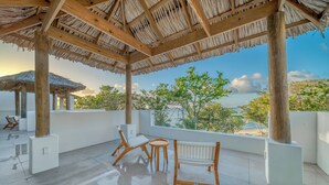A covered outdoor seating area with wooden furniture and a view of the sea.