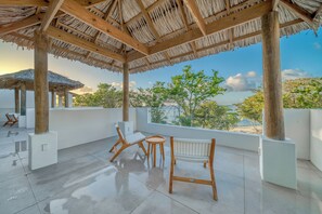 A covered outdoor seating area with wooden furniture and a view of the sea. - Elevated Island Escape – Studio Condo with Ocean Views (Roatán)