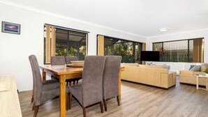 Un salon moderne avec une table à manger en bois, des chaises à revêtement gris, un canapé beige et un téléviseur.