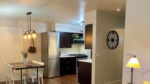 A modern kitchen with stainless steel appliances, a dining area with white chairs, and a wooden floor. - Charming Bungalow 2 in lovely Spearfish with WiFi, AC (Spearfish)