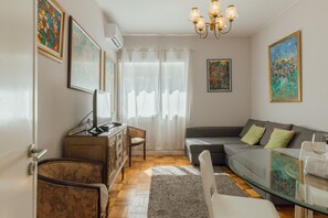A living room with a sofa, a glass coffee table, a television on a wooden cabinet, and artwork on the walls. - DOWNTOWN AQUARELLE with AC by VACATIONY (Oporto)