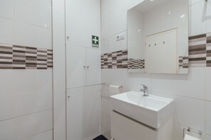 A bathroom with white tiles, a sink, a mirror, and a sign indicating first aid. - DOWNTOWN AQUARELLE with AC by VACATIONY (Oporto)