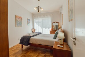 A bedroom with a bed, a bedside table, a lamp, a chair, a window with curtains, and a ceiling light. - DOWNTOWN AQUARELLE with AC by VACATIONY (Oporto)