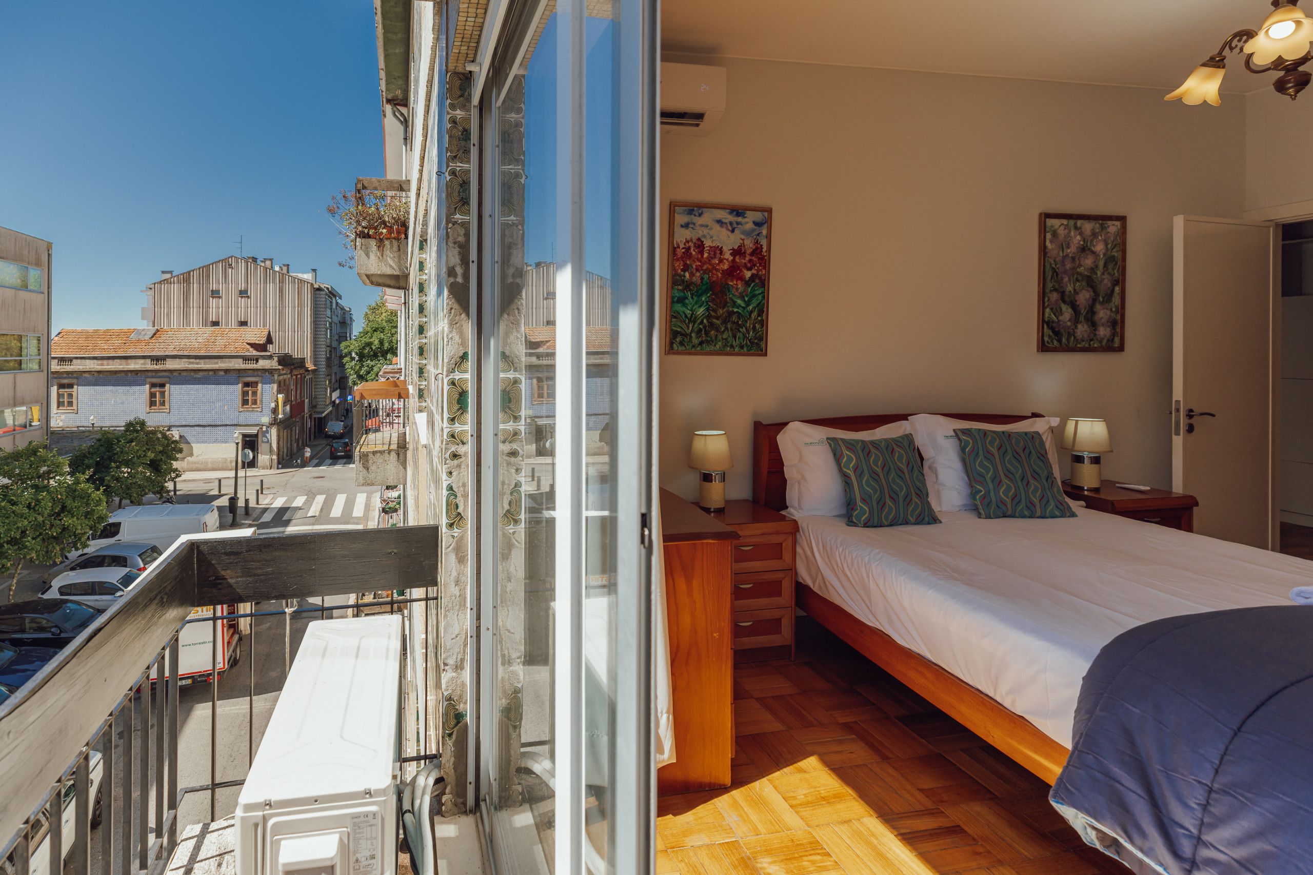 A hotel room with a bed, bedside tables, and a view of the city.