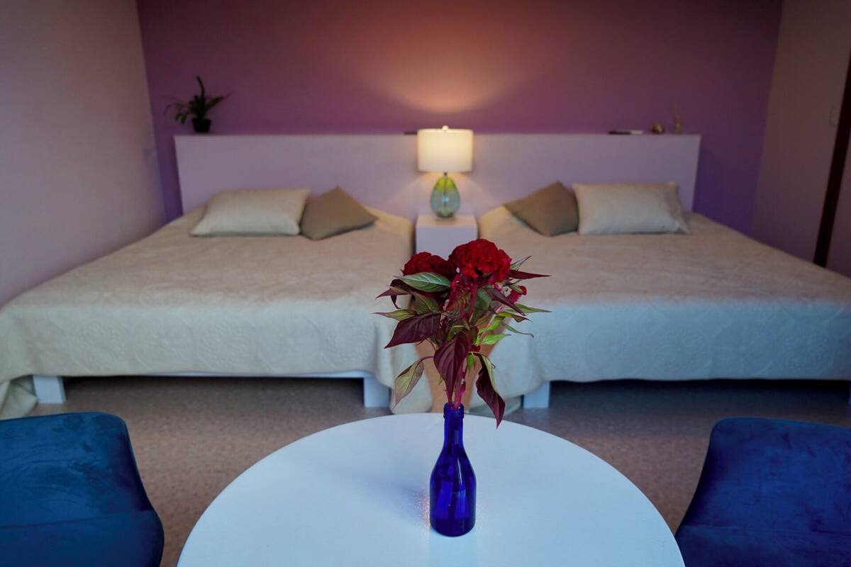A hotel room with a bed, a bedside table with a vase of flowers, and a lamp on the wall.