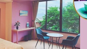 Ein gemütliches Zimmer mit großem Fenster, einem Schreibtisch, zwei Stühlen und einem Bett.