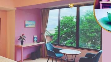 Ein gemütliches Zimmer mit großem Fenster, einem Schreibtisch, zwei Stühlen und einem Bett.