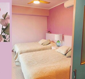 A hotel room with two beds, a ceiling fan, a nightstand with a lamp, and a wall-mounted air conditioner. - Hotel MOANA (Oshima)