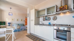 A modern kitchen with white cabinets, a gas stove, and a built-in oven. There is a dining area with a table and chairs, and a patterned rug on the floor.