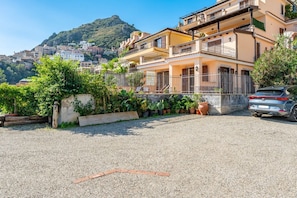 A residential building with balconies, a gravel driveway, and a car parked in front.