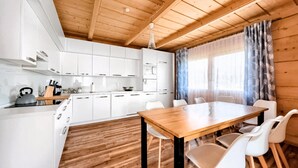 Moderni keittiö, jossa on valkoiset kaapit, puinen ruokapöytä ja suuri ikkuna, jossa on verhot.