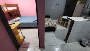 A dormitory room with bunk beds, a single bed, a desk, a chair, a small table, and a trash bin.