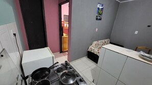 A compact kitchen with a gas stove, pots, a white refrigerator, and a small dining area with a floral tablecloth.