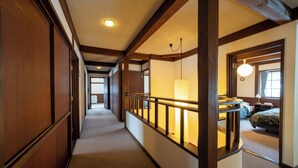A hotel corridor with wooden paneling, a carpeted floor, a railing, and a bed in the adjacent room. - Cottage Alice (Hachimantai)