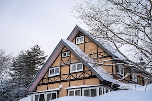 Un chalet traditionnel doté d’un toit à forte pente, de nombreuses fenêtres et d’une façade recouverte de neige.