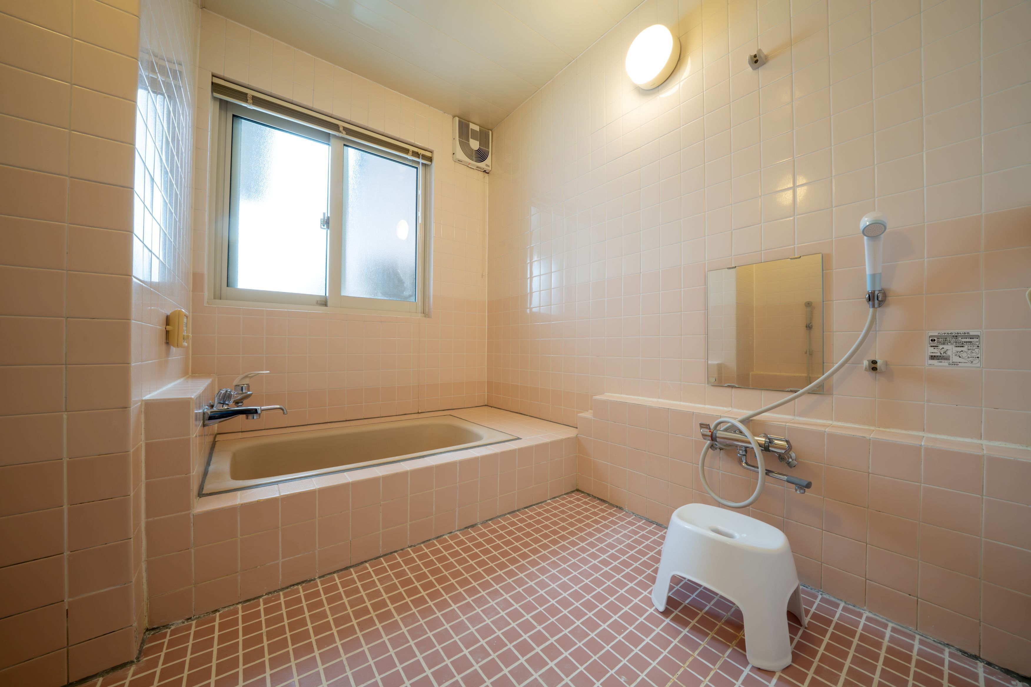 Een badkamer met een badkuip, een klein krukje, een raam en een spiegel.