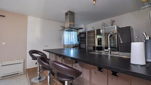 A modern kitchen with a stainless steel countertop, a built-in oven, a sink, and two bar stools. - Beautiful home in Sainte Maxime (Sainte Maxime)