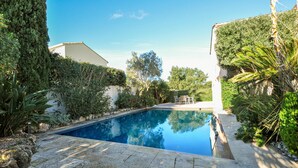 A swimming pool with a stone deck, surrounded by lush greenery and a white building. - Beautiful home in Sainte Maxime (Sainte Maxime)