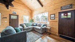 A log cabin interior with a sectional sofa, a welcome sign, and a bear head on the wall. - Bear's Den Retreat • Hot Tub • Soak Tub • Dog Friendly • Hocking Hills Cabin (Logan)