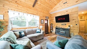A cozy cabin interior with a sofa, a television, and a fireplace. - Bear's Den Retreat • Hot Tub • Soak Tub • Dog Friendly • Hocking Hills Cabin (Logan)