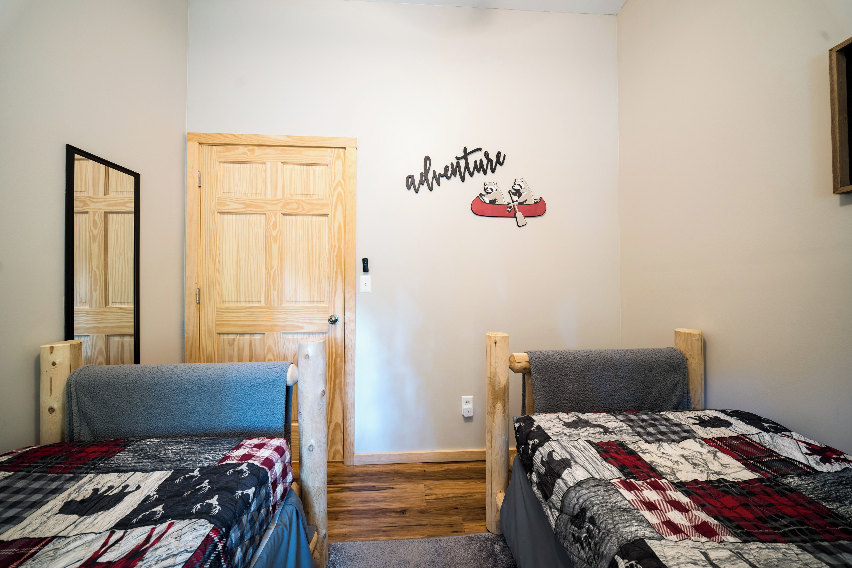 Quarto com duas camas, uma porta de madeira e um objeto decorativo na parede.