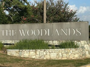 A sign for 'The Woodlands' with a stone wall and greenery in front.