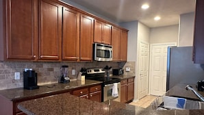 A kitchen with granite countertops, stainless steel appliances, wooden cabinets, and a tiled backsplash.