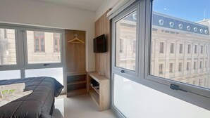 A modern bedroom with a bed, a TV, and a large window offering a view of a building. - Luxury In Best Area San Telmo (Buenos Aires)