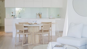 A modern kitchen with white cabinetry, a dining table with four chairs, and a white sofa in the living area.