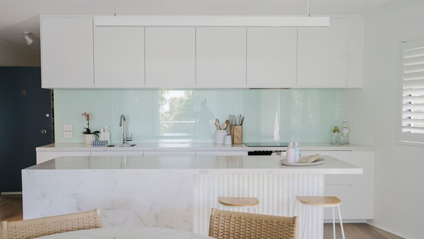 A modern kitchen with white cabinetry, a marble island, and a dining area with wicker chairs.