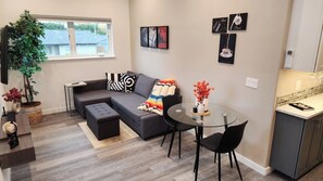 Een moderne woonkamer met een grijze bank, een glazen salontafel en een eethoek. Er staat een potplant en een wereldbol op een houten tafel.