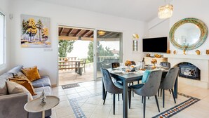 Un salon moderne avec un canapé, une table à manger et des chaises. On y trouve une cheminée, un téléviseur et une grande fenêtre.