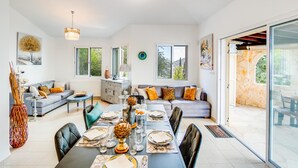 Un espace repas moderne avec une longue table dressée pour six personnes, entourée de canapés et d’un meuble.
