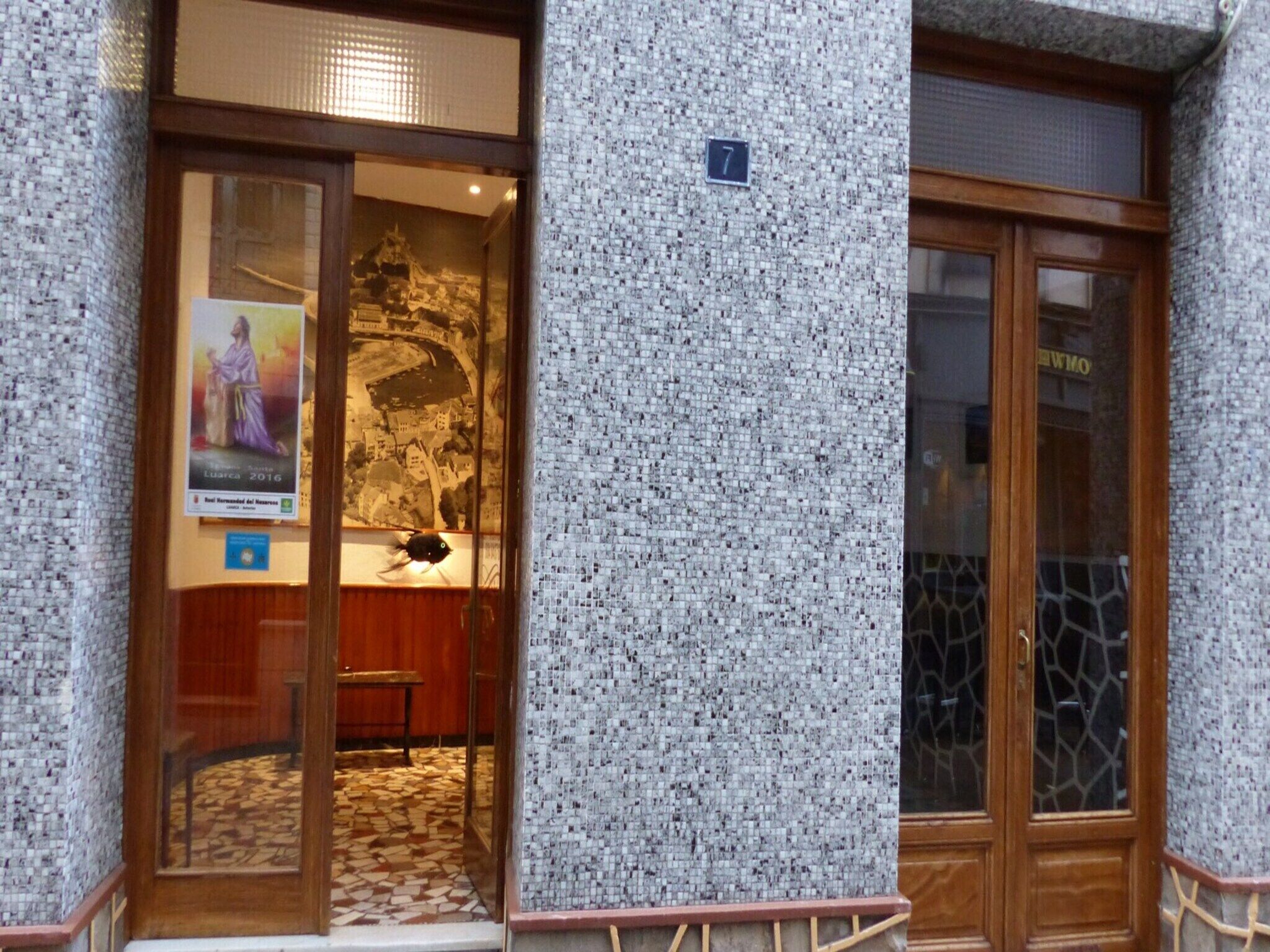 Une entrée d’immeuble avec un mur décoré d’une mosaïque, une porte en bois et une affiche à l’intérieur.