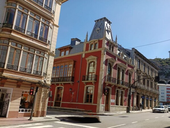 Une vue de rue d’un bâtiment doté d’une tour horloge, de grandes fenêtres et d’une façade rouge.