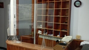 A reception desk with a wooden finish, a glass partition, and a telephone. Behind the desk, there is a wooden shelving unit with numbered compartments. - Room-cozy Double Room With Shared Bathro (Valdes)