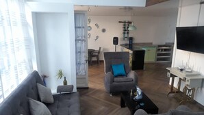 Una sala de estar moderna con un sofá, un sillón y una mesa de centro. Se ve, al fondo, una zona de comedor con una mesa y sillas.