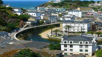 A coastal town with a prominent white building, a curved road, and a lighthouse in the background.