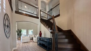 A spacious living area with a wooden staircase, a white sofa, and a blue console table.