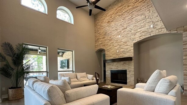 A spacious living room with a stone accent wall, large windows, and a fireplace.