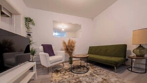Un salon moderne avec un téléviseur à écran plat, un canapé vert, un fauteuil blanc et une petite table basse ronde.