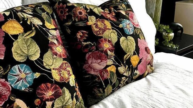 Un lit avec du linge de lit blanc et un coussin à motifs floraux noirs.