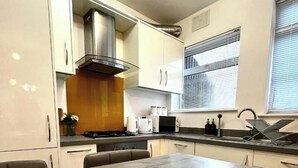 Une cuisine compacte avec des meubles blancs, une hotte de cuisinière en acier inoxydable, un four encastré, un four à micro-ondes et un évier.
