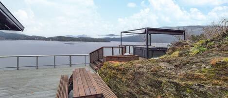 A wooden deck with benches overlooking a lake, a covered seating area, and a view of distant mountains.