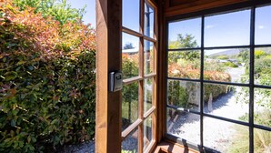 Una habitación con un ventanal grande, una puerta de madera y vistas a un jardín con arbustos y árboles.